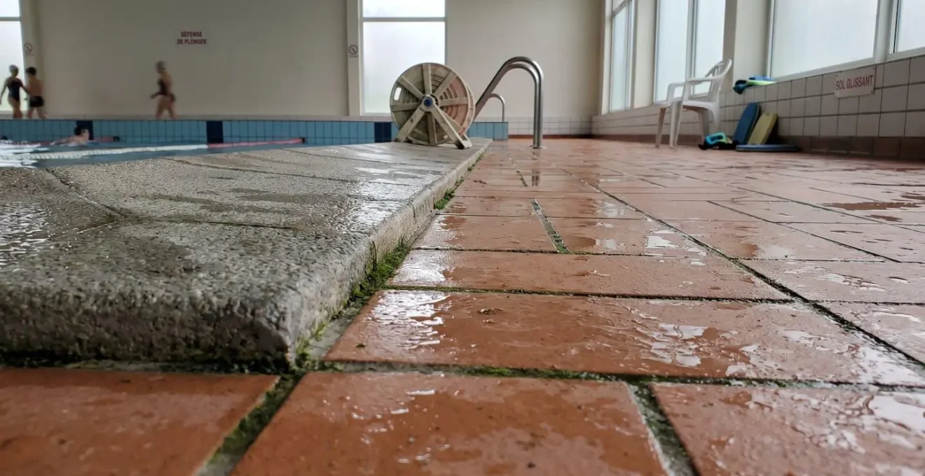 Margelles de piscine et sol environnant présentant des traces d'humidité persistantes et flaques d'eau