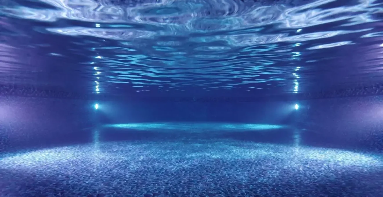 Vue sous-marine d'une piscine illuminée par des LED bleues et violettes la nuit.